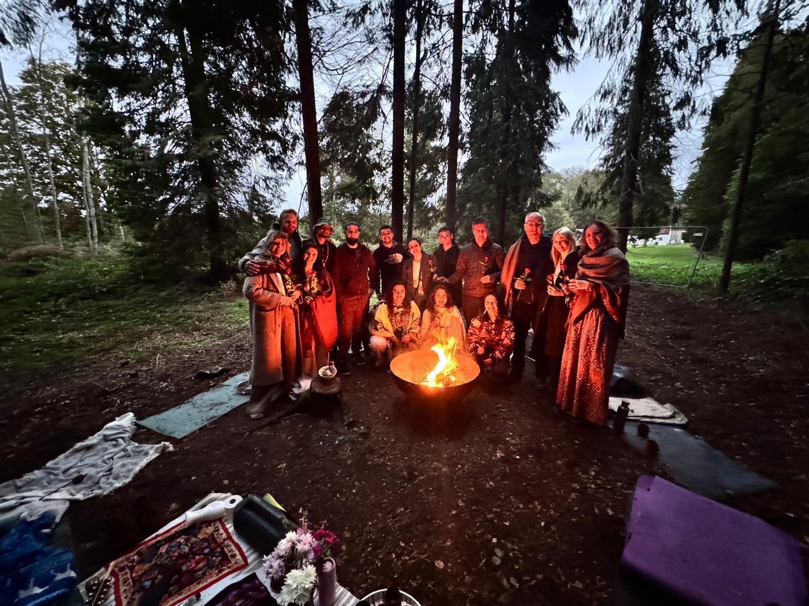 A group gathered around a fire at dusk for an evening cacao ceremony in the woods