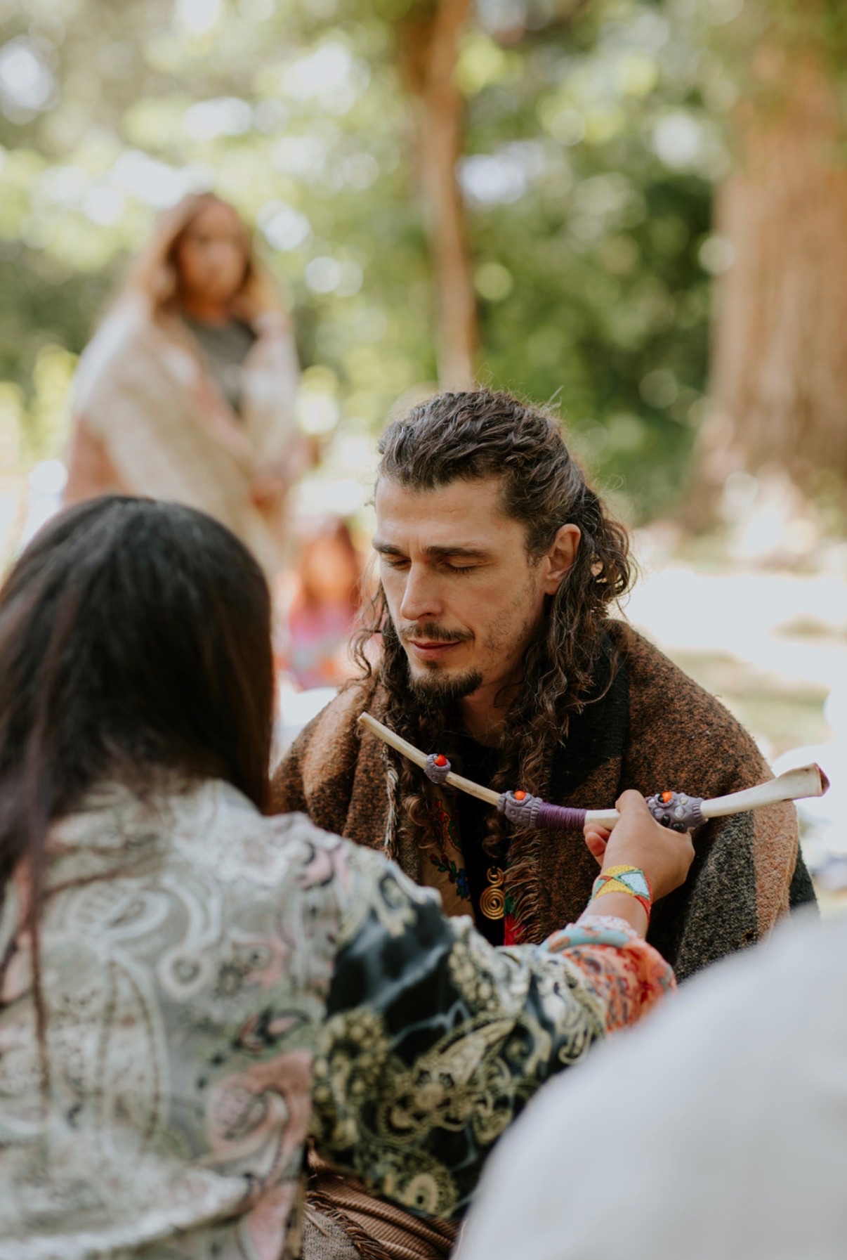 A guest receiving hape through a tepi pipe under the trees at a cacao and hape ceremony