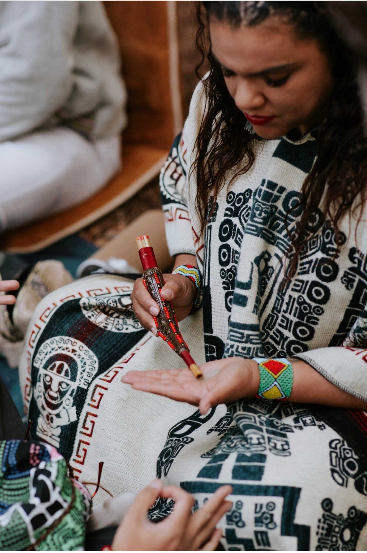 Katie preparing hape with a tepi applicator, seated on a patterned blanket at a private ceremony